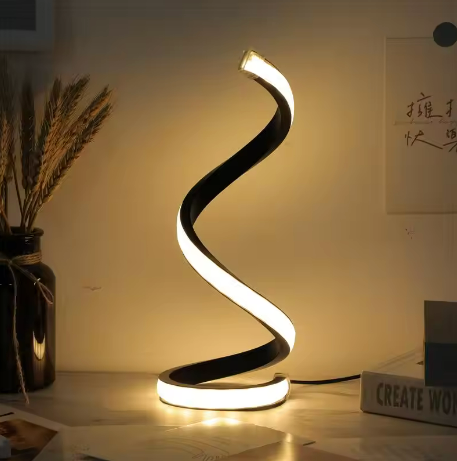 Spiral LED table lamp lit warm on desk — about 2½ twists, matte black